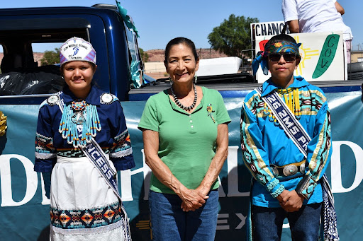 Deb Haaland and two people dressed in traditional garments stand next to a truck